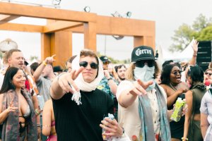 Two college aged people pointing at the camera while a crowd dances behind.